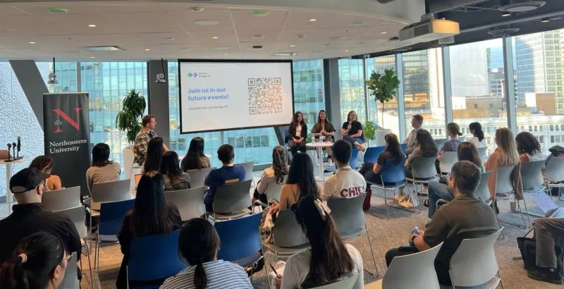 A three-person panel in front of a full room at I am a Service Designer, Ask Me Anything, with a Northeastern University banner beside them